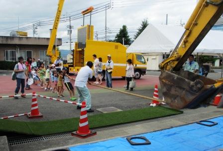 写真：【バックホウと綱引きする参加者たち】