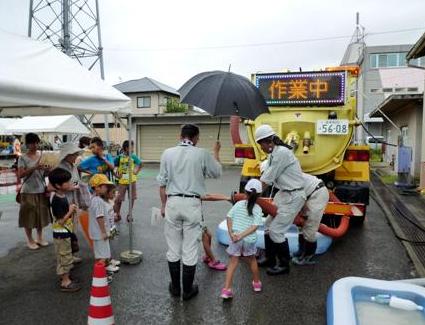 写真：【側溝清掃車の説明を受けている参加者たち】